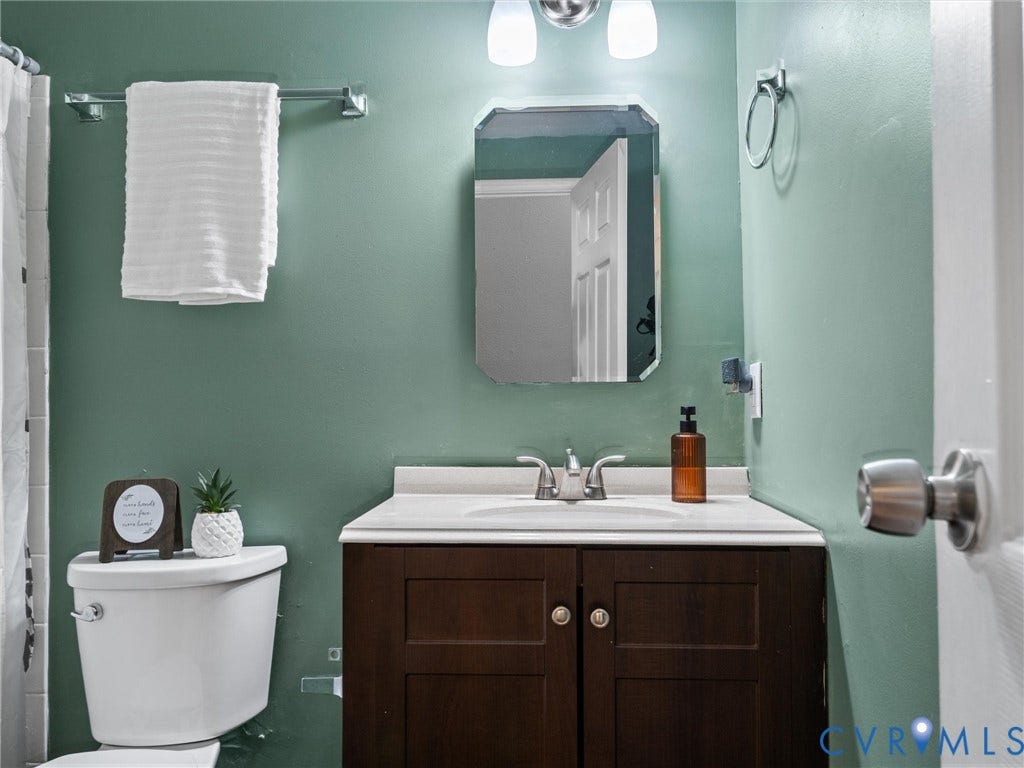 2703 Sutters Mill Court, Sutters Mill, Chesterfield, VA 23112 Dark wood-finish vanity with an integrated sink and countertop, polished chrome hardware, beveled wall-mounted mirror, and dual-light vanity fixture