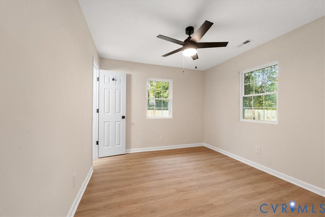 524 St Matthew Street, The Heights, Petersburg, VA 23803 Neutral-toned interior space featuring light wood-finish flooring, dual-pane windows, a six-panel door, and a matte black ceiling fan with an integrated light fixture