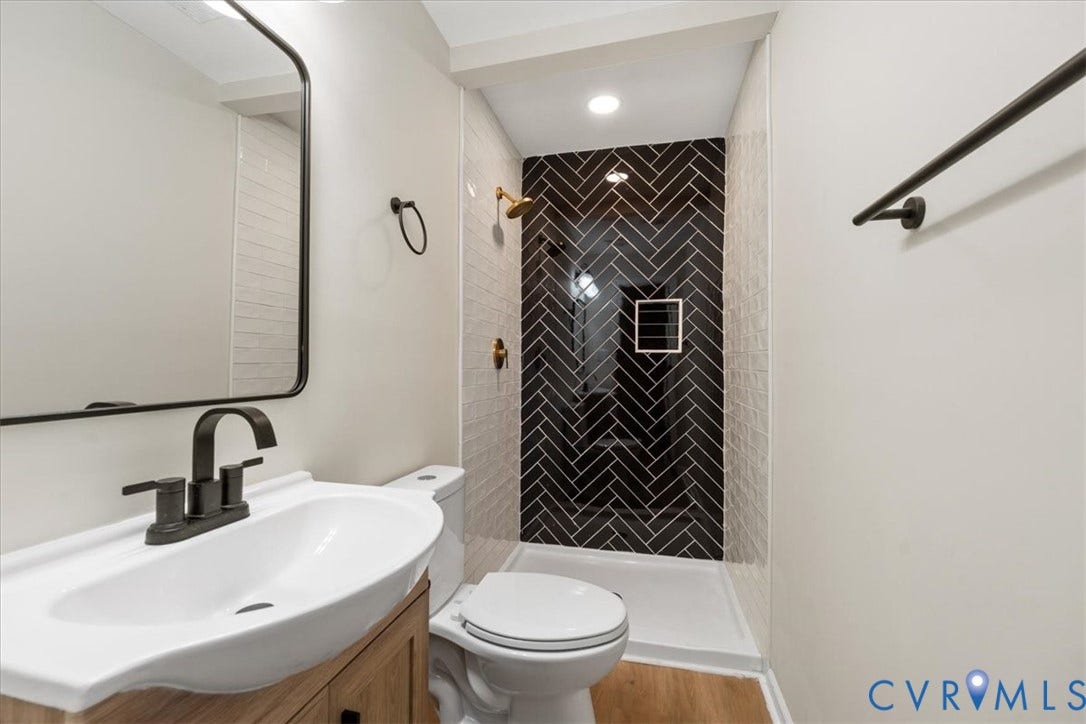 524 St Matthew Street, The Heights, Petersburg, VA 23803 Bathroom featuring a walk-in shower with black herringbone-patterned tile, wood-finish vanity with white basin, matte black hardware, and an arched-frame mirror