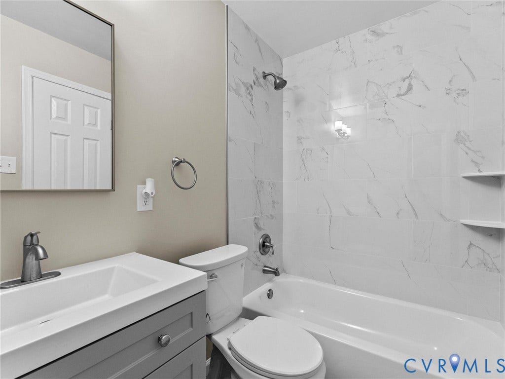 3303 Jowin Lane, Henrico, VA 23223 Bathroom featuring a gray vanity with a rectangular sink, wall-mounted mirror, tub-shower combination with light-veined tile surround, and integrated shelving