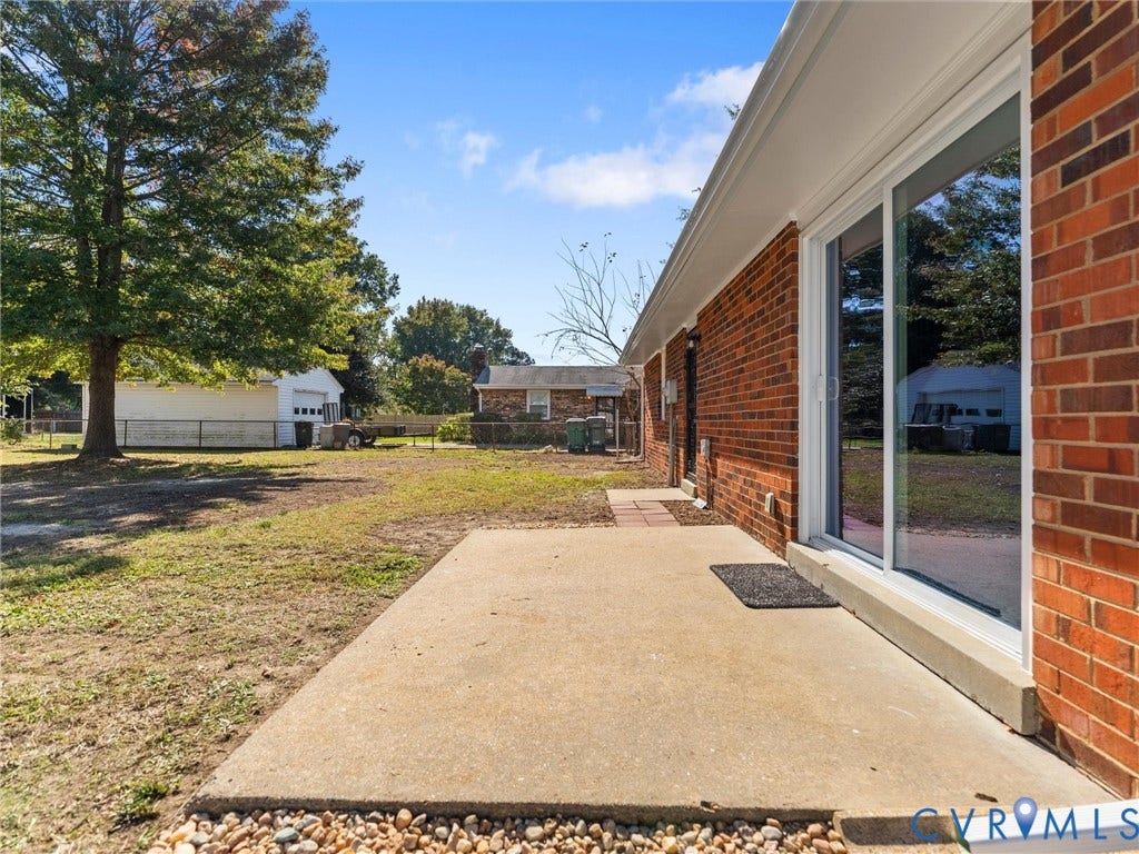 3303 Jowin Lane, Henrico, VA 23223 Red brick exterior featuring a concrete patio, sliding glass door, and expansive rear grounds with mature trees