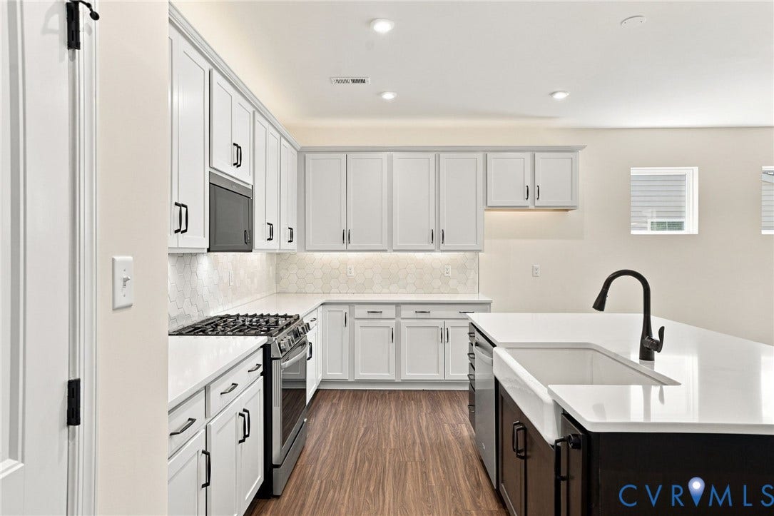 7712 Hawthorne Avenue, Henrico, VA 23227 Kitchen featuring white shaker-style cabinetry, a contrasting dark kitchen island, solid-surface countertops, a farmhouse-style sink with a matte black faucet, and patterned backsplash tile