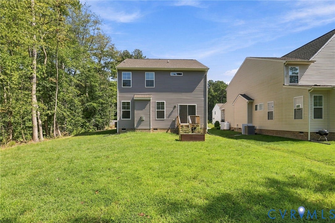 7712 Hawthorne Avenue, Henrico, VA 23227 Rear exterior featuring horizontal vinyl siding, multi-level windows, a sliding glass door, and an attached wood deck overlooking a grassy lawn with mature tree coverage