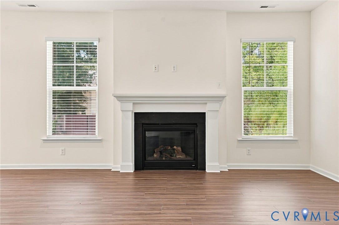 7712 Hawthorne Avenue, Henrico, VA 23227 Fireplace with a black surround and white mantel, flanked by dual windows with blinds and wood-finish flooring