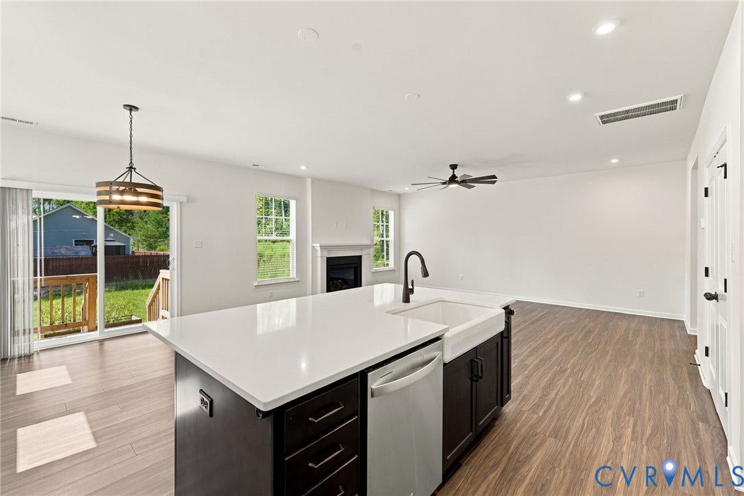 7712 Hawthorne Avenue, Henrico, VA 23227 Kitchen island featuring a white surface, dark cabinetry, and an apron-front sink, wood-finish flooring, recessed lighting, and a fireplace with a decorative mantel