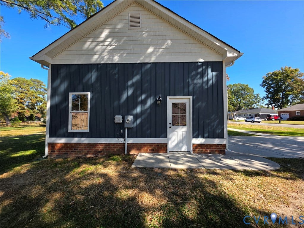 3005 Portsmouth Street, Hopewell, VA 23860 Exterior featuring vertical board-and-batten siding, shake shingle gable, brick base, concrete pad, and white-trim door