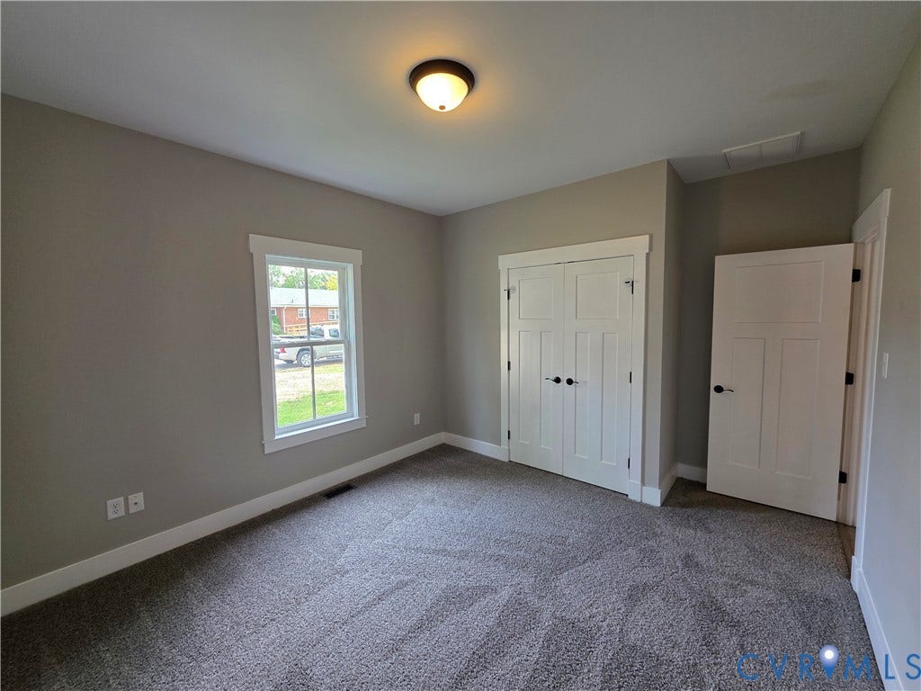 3005 Portsmouth Street, Hopewell, VA 23860 Room featuring neutral-toned walls, carpeting, a single-pane window with white trim, a double-door closet with shaker-style panels, and a flush-mount ceiling light fixture