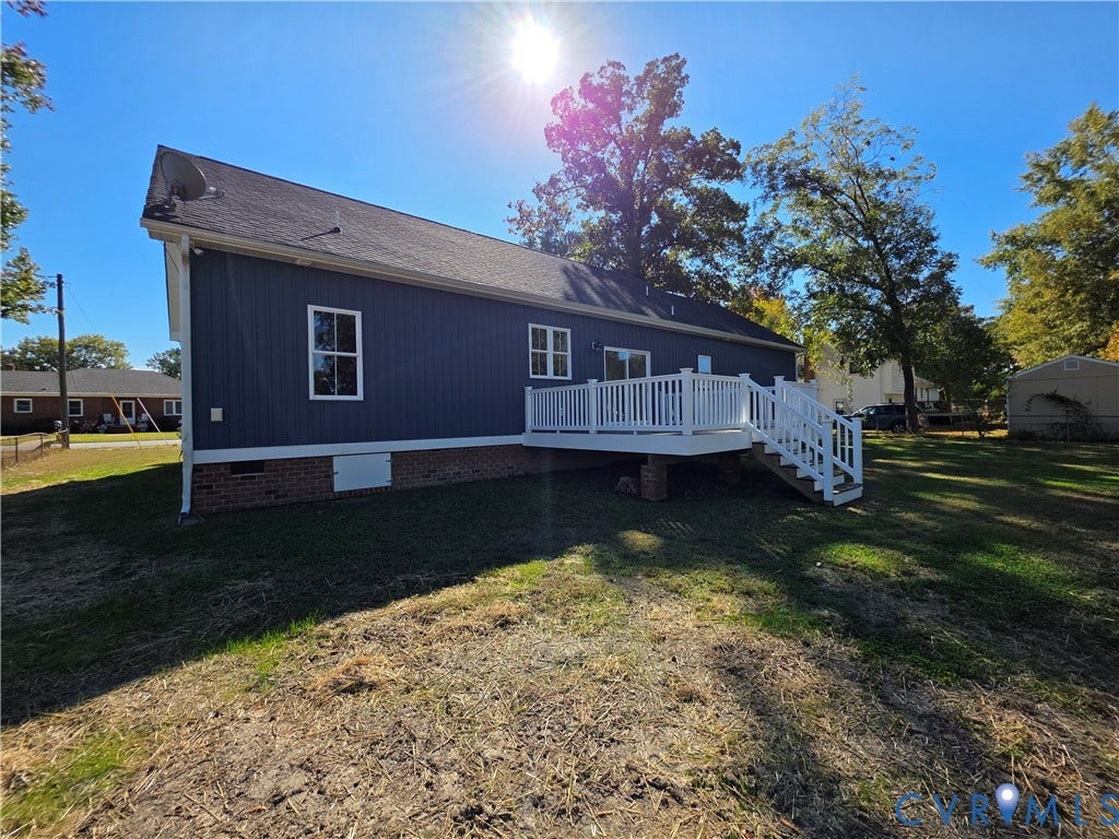 3005 Portsmouth Street, Hopewell, VA 23860 Exterior featuring vertical blue siding, brick masonry foundation, elevated white deck with railing, and mature trees on the grounds