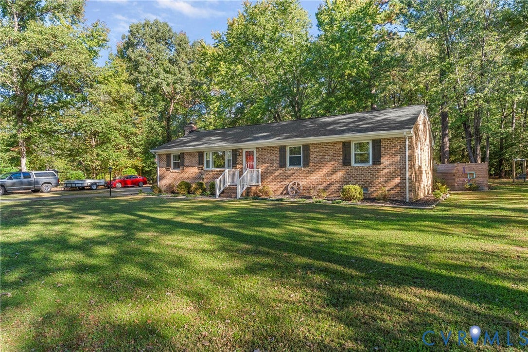 8444 New London Road, Mechanicsville, VA 23116 Single-story brick exterior featuring a shingled gable roof, expansive lawn, white railing entrance, and dense perimeter tree canopy
