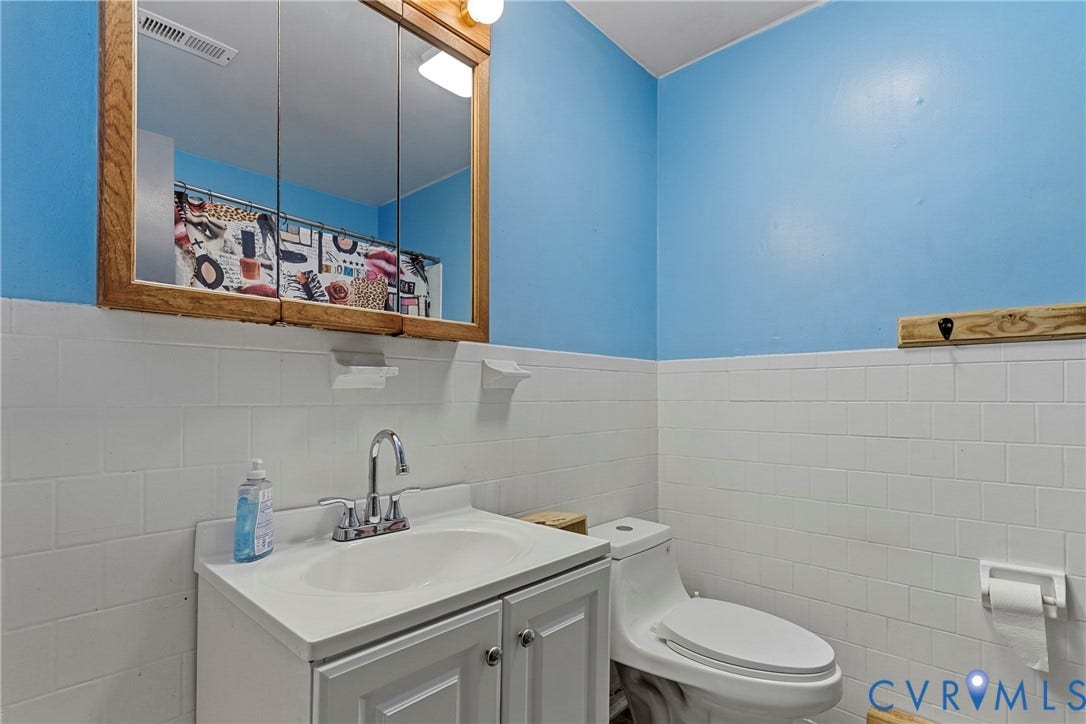 8444 New London Road, Mechanicsville, VA 23116 Bathroom featuring white subway tile wainscoting, white vanity with integrated basin and chrome faucet, wood-framed medicine cabinet, and white toilet