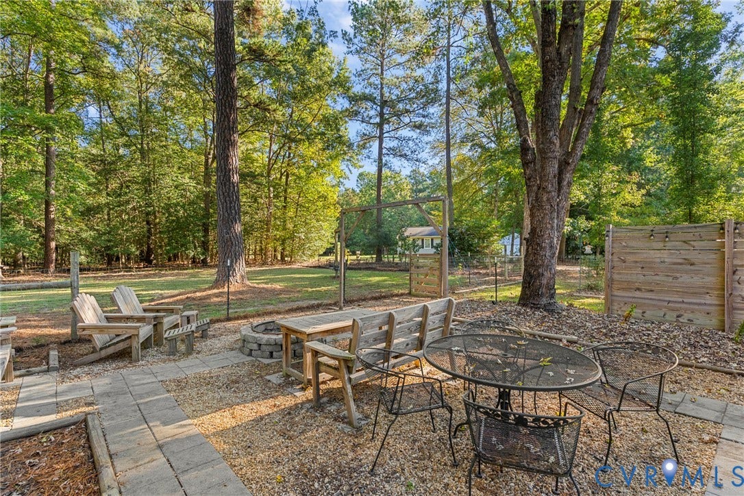 8444 New London Road, Mechanicsville, VA 23116 Backyard featuring a paved stone patio, built-in stone fire pit, wood-slat privacy fencing, and mature trees