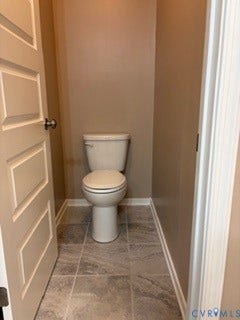 2144 Perennial Circle, Henrico, VA 23233 Solid-core panel door featuring satin nickel hardware, tile flooring with stone-finish patterning, and a high-profile toilet
