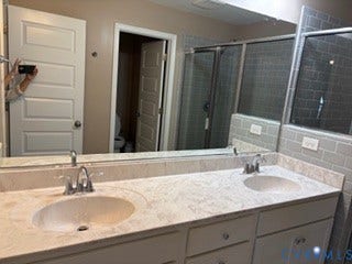 2144 Perennial Circle, Henrico, VA 23233 Dual-sink vanity featuring stone-finish countertops with integrated basins, chrome fixtures, cabinetry storage, and gray subway tile shower surround
