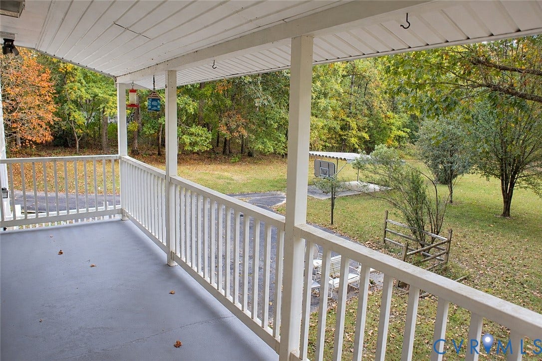 9711 Old Stage Road, Prince George, VA 23875 Covered porch featuring painted flooring and white structural railings, overlooking a wooded yard with mature trees