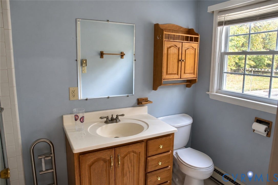 9711 Old Stage Road, Prince George, VA 23875 Bathroom featuring a wood vanity with integrated countertop and sink, wall-mounted wood cabinetry, a rectangular mirror, and a window with blinds