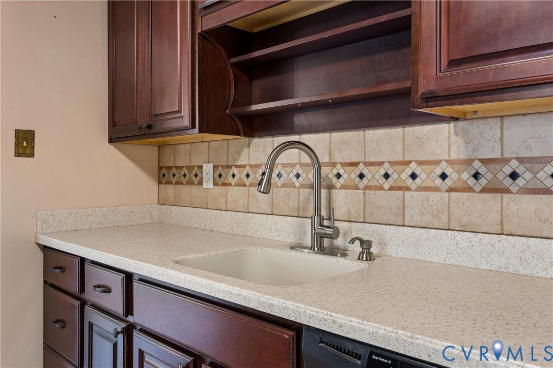 627 Sedgefield Drive, 992- All Others Area 107, Newport News, VA 23605 Dark wood-finish cabinetry featuring open shelving, light-toned composite countertop, integrated sink with a stainless steel gooseneck faucet, and decorative tile backsplash with diamond-pattern accents