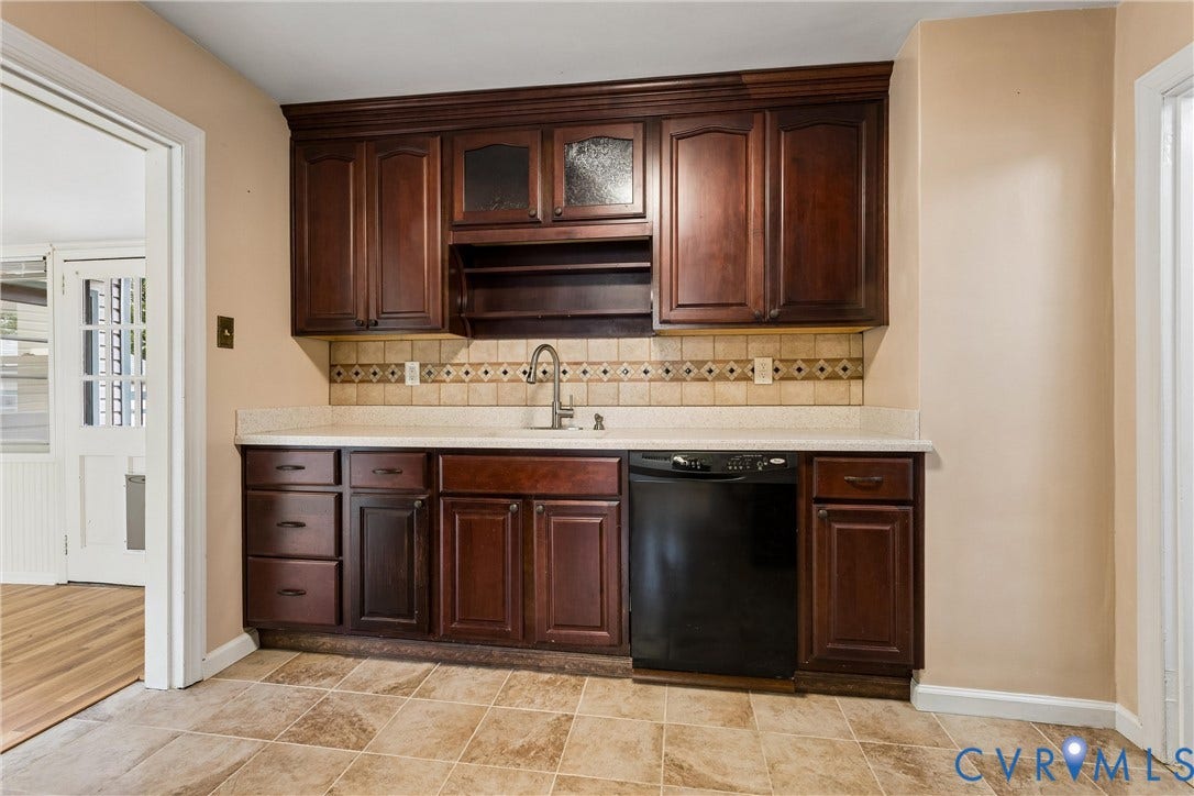 627 Sedgefield Drive, 992- All Others Area 107, Newport News, VA 23605 Dark wood cabinetry with glass-front accents, solid surface countertops, patterned ceramic tile backsplash, integrated undermount sink with gooseneck faucet, and stone-finish tile flooring
