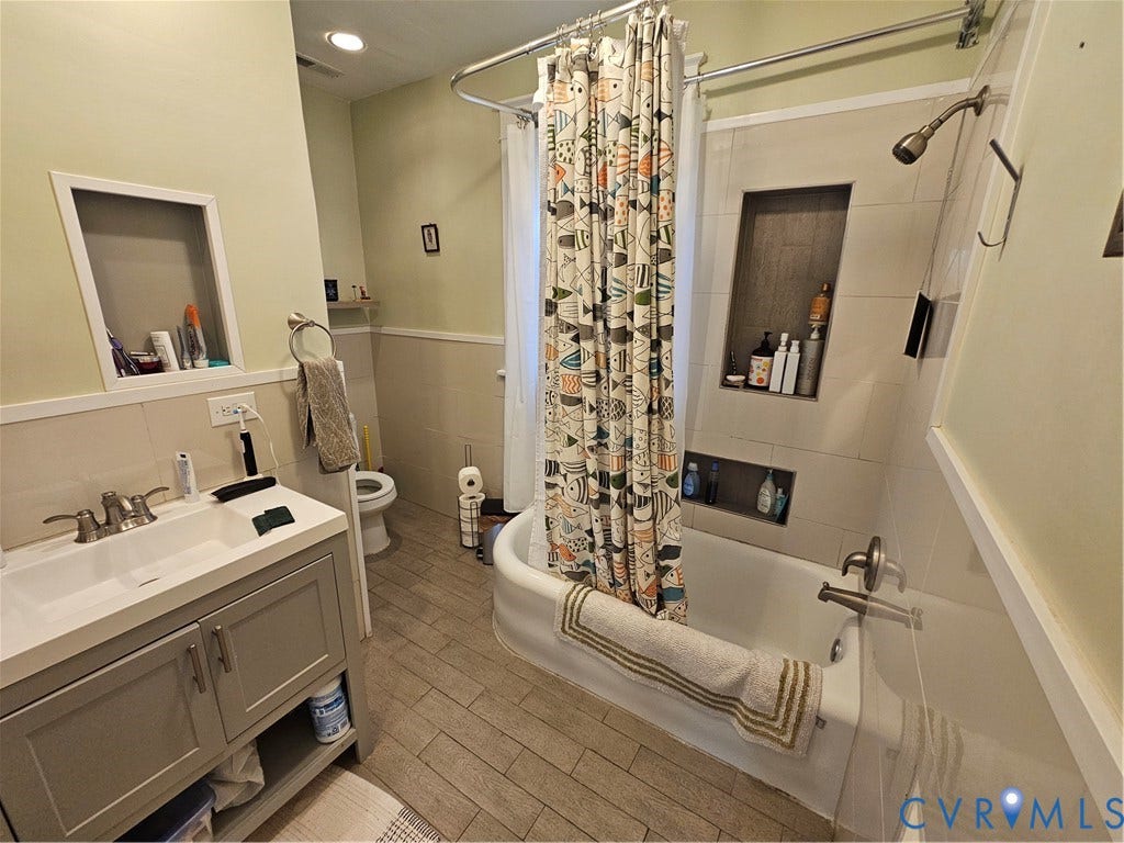 1206 Westminster Avenue, Richmond, VA 23227 Bathroom featuring a gray vanity with integrated sink, tile-surround tub with dual recessed niches, wood-finish flooring, and wainscoting
