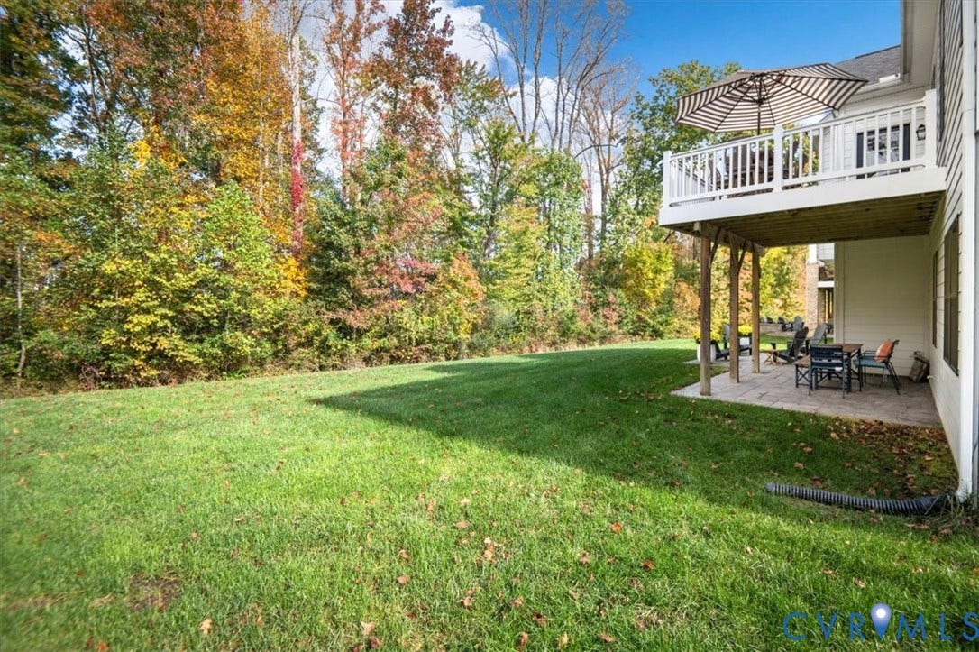 12168 Readers Pointe Drive, Readers Branch, Goochland, VA 23103 Rear exterior featuring an elevated wood deck with white railings, a paved stone patio, and an expansive lawn bordered by mature trees