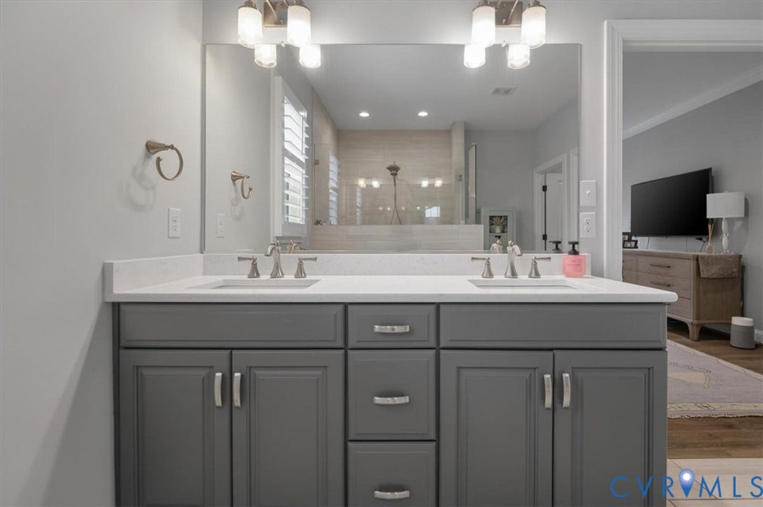 12168 Readers Pointe Drive, Readers Branch, Goochland, VA 23103 Dual-sink vanity with a solid-surface countertop, cabinetry in a grey finish, brushed nickel hardware, and dual-bulb wall-mounted lighting fixtures