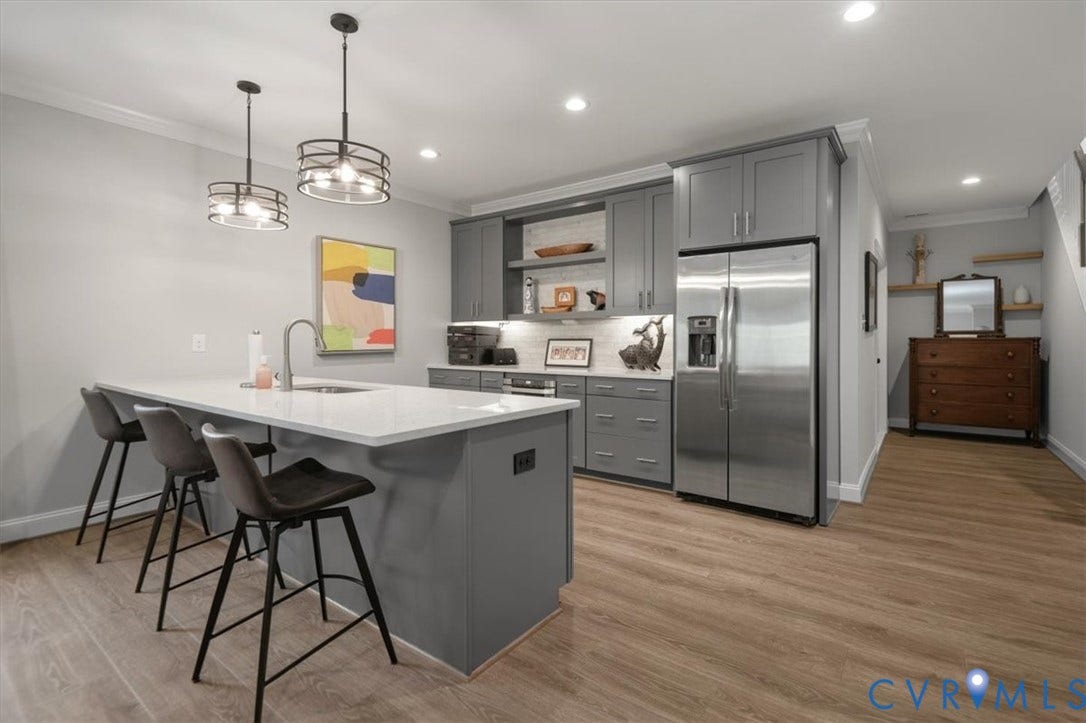 12168 Readers Pointe Drive, Readers Branch, Goochland, VA 23103 Terrace Level Kitchen featuring a central island with a stone countertop and integrated sink, gray cabinetry, stainless steel refrigerator, wood-finish flooring, and dual hanging pendant light fixtures