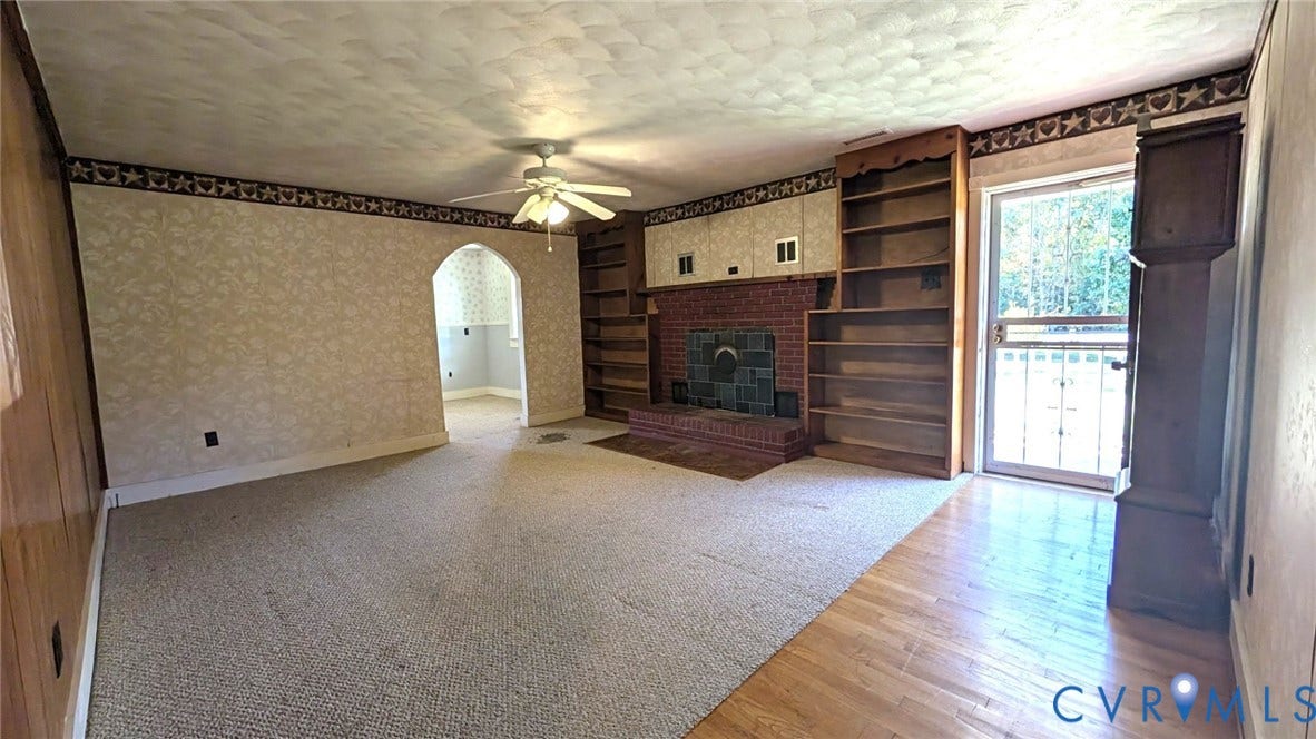 8893 King William Road, King William, VA 23009 Brick fireplace with integrated shelving, ceiling-mounted fan, arched doorway, and glass-paneled exterior door