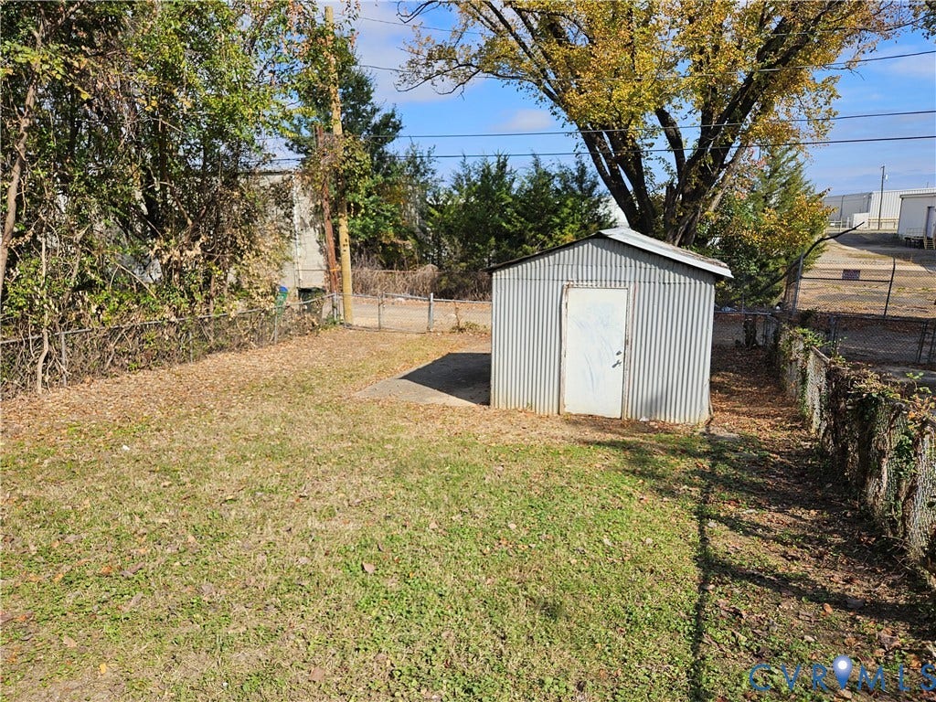 1112 E 15th Street, Richmond, VA 23224 Rear yard featuring a corrugated metal storage shed, concrete pad, chain-link fencing, and mature trees