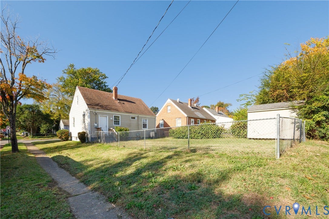 1010 E 17th Street, Oak Grove, Richmond, VA 23224 Exterior view featuring a light-colored siding finish, a gable roofline with brick chimneys, and a chain-link fenced yard with a detached storage structure