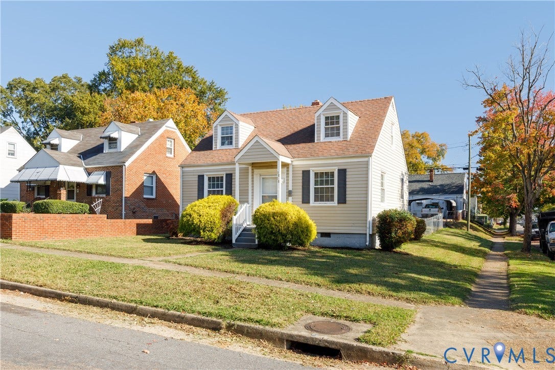1010 E 17th Street, Oak Grove, Richmond, VA 23224 Cape Cod exterior featuring a beige siding finish, twin dormer windows, an asphalt shingle roof, dark window shutters, and a covered front entryway
