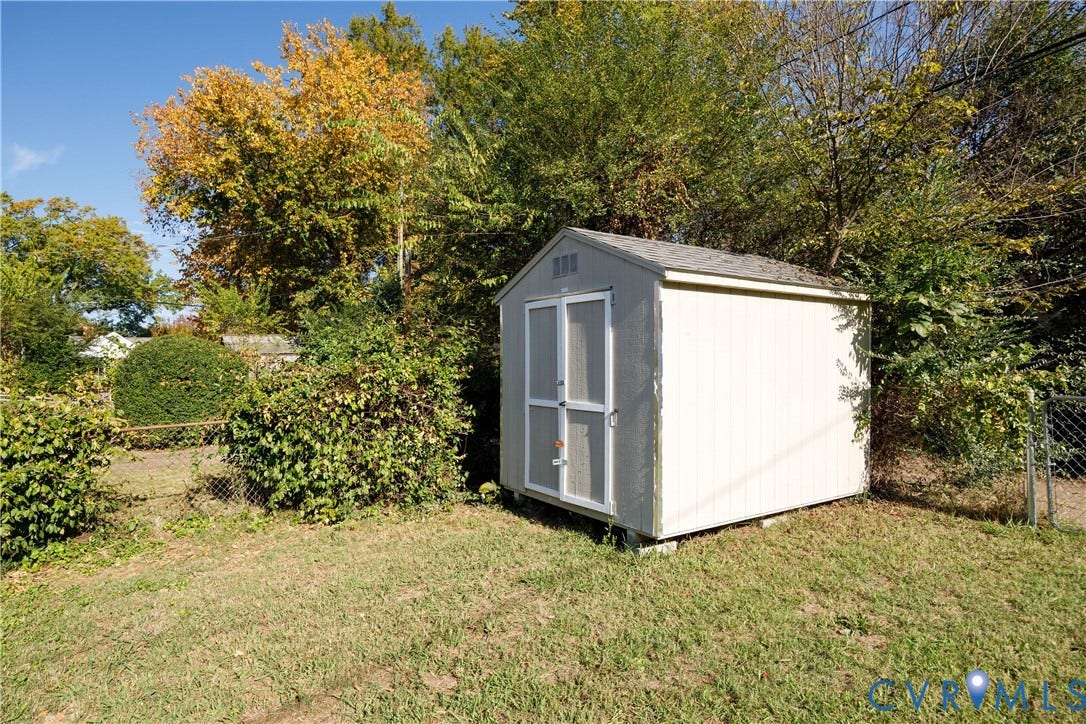 1010 E 17th Street, Oak Grove, Richmond, VA 23224 Outdoor storage structure featuring light-colored siding, double doors, and a gabled roof set on a level lawn with perimeter fencing