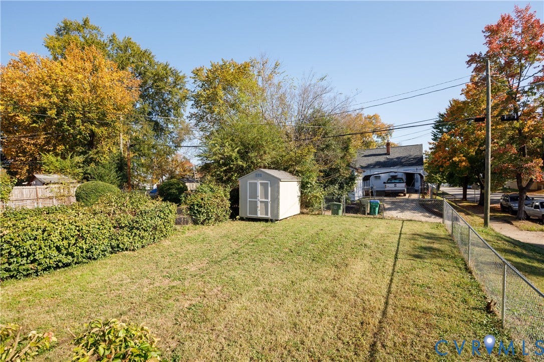 1010 E 17th Street, Oak Grove, Richmond, VA 23224 Backyard featuring a grass lawn, chain-link fencing, a detached storage shed, mature trees, and a gravel driveway