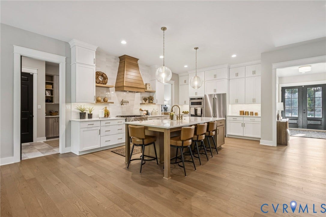 9275 Topeka Road, Quinton, VA 23141 Expansive kitchen featuring a large central island, white cabinetry, integrated stainless steel appliances, a wood-finish range hood, and light wood-finish flooring