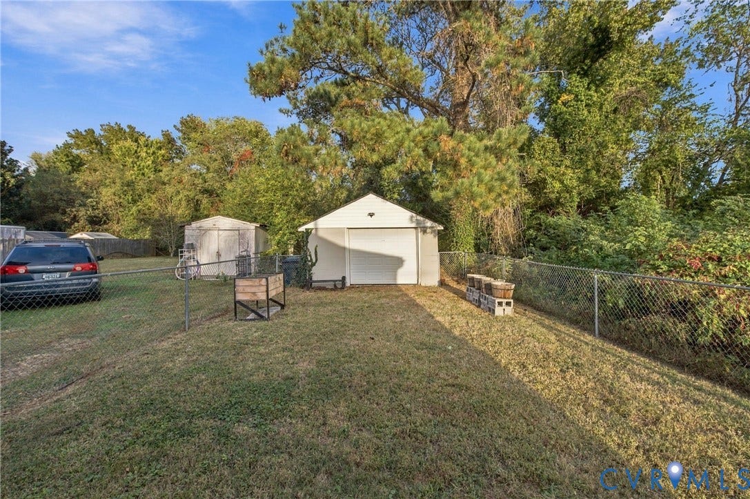 20 Victor Street, Geo Moss Estate, Hampton, VA 23669 Detached single-car garage featuring a white door, accompanied by a secondary storage shed and chain-link fencing within a grass-covered backyard