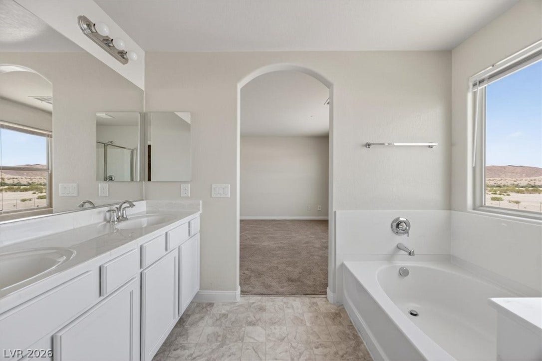 1116 Strada Cristallo, Henderson, NV 89011 The bright bathroom features a spacious soaking tub, double vanity, and views of distant hills.