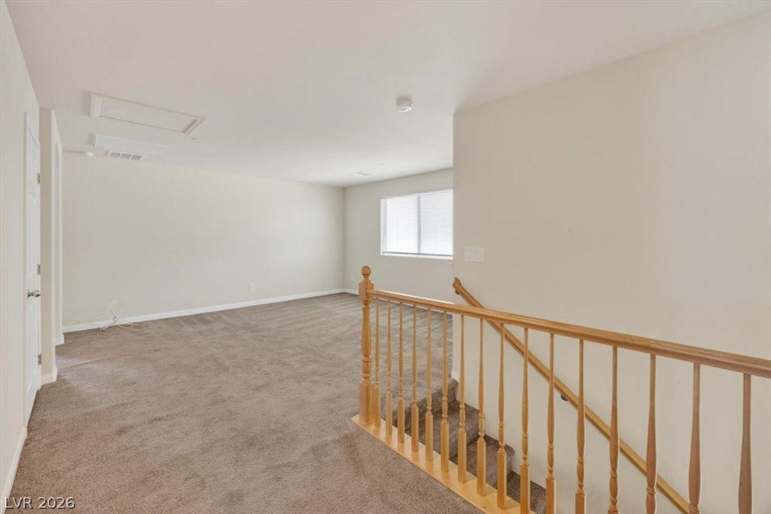 1116 Strada Cristallo, Henderson, NV 89011 A warm, neutral carpeted room with a bright window and classic wooden stair railing.