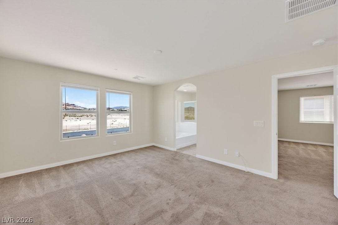 1116 Strada Cristallo, Henderson, NV 89011 A spacious primary bedroom featuring plush carpeting and large windows with desert mountain views.