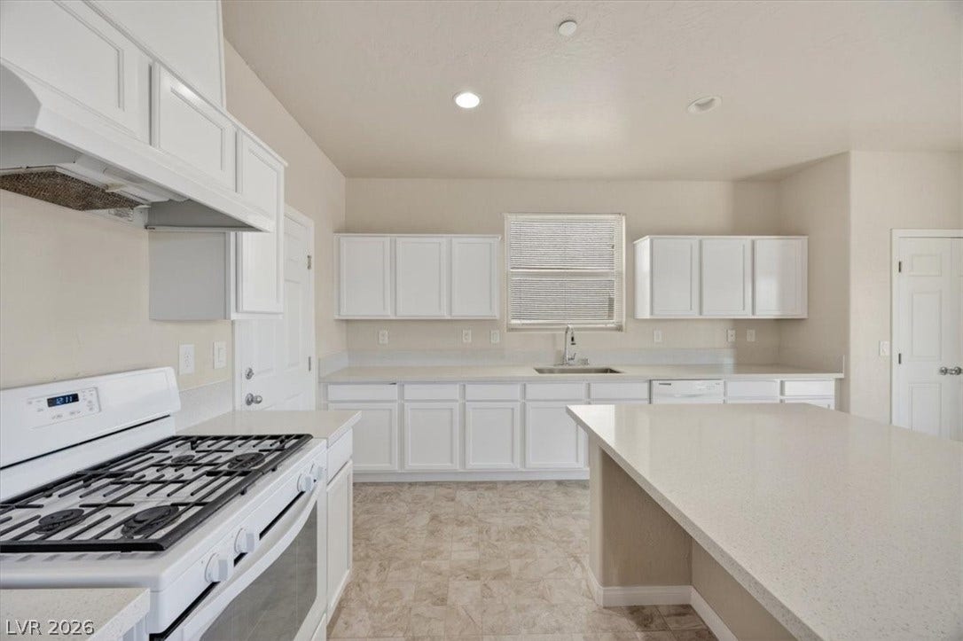 1116 Strada Cristallo, Henderson, NV 89011 White cabinetry and stone countertops elevate this kitchen, complete with modern appliances.