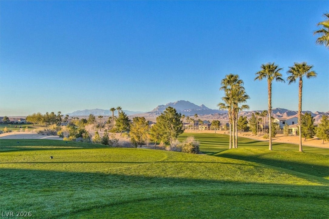 1116 Strada Cristallo, Henderson, NV 89011 Green fairways stretch towards a rugged mountain range under an azure sky, framed by slender palm trees.