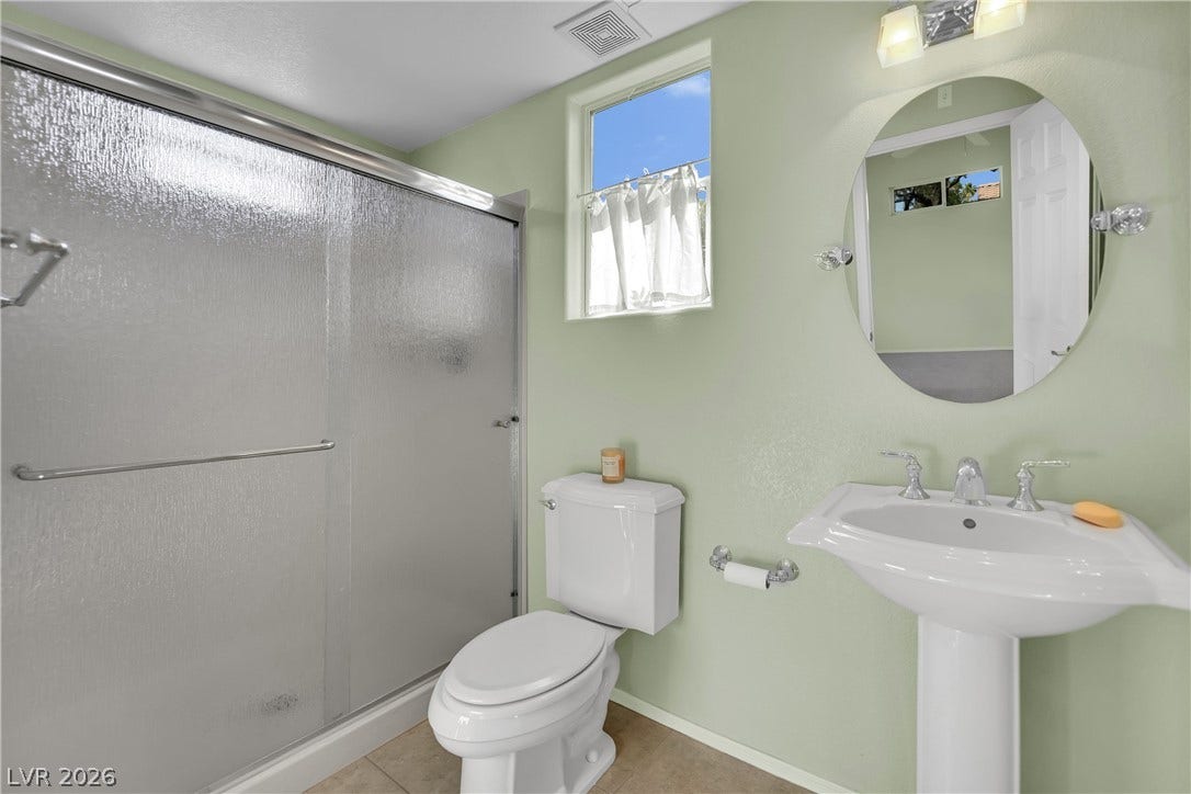 This bright bathroom features a pedestal sink and a shower with sliding glass doors.