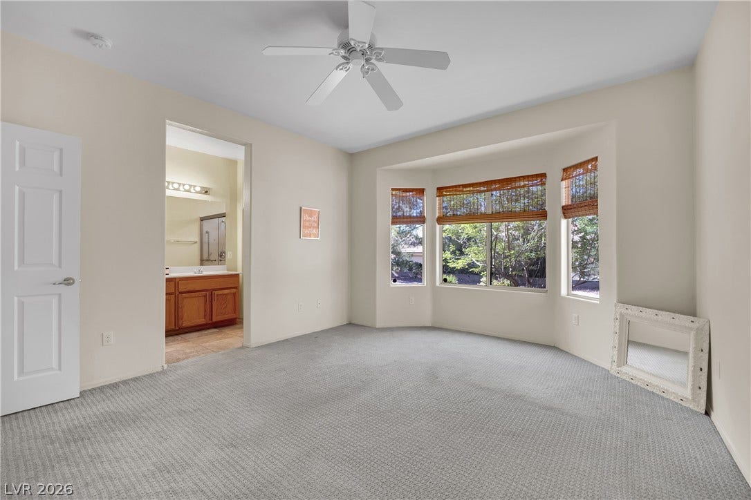 This spacious primary bedroom features carpet flooring and a bay window overlooking lush trees.