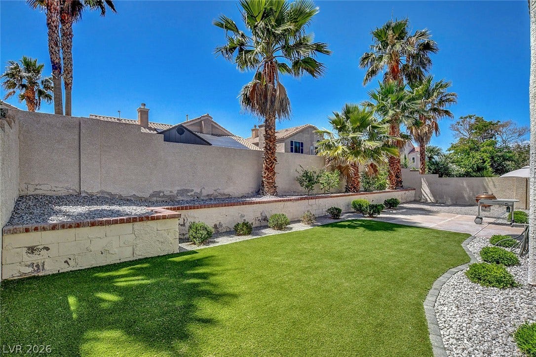 31 Antero Drive, Henderson, NV 89074 A private yard with vibrant green artificial turf, surrounded by mature palm trees and low-maintenance landscaping.