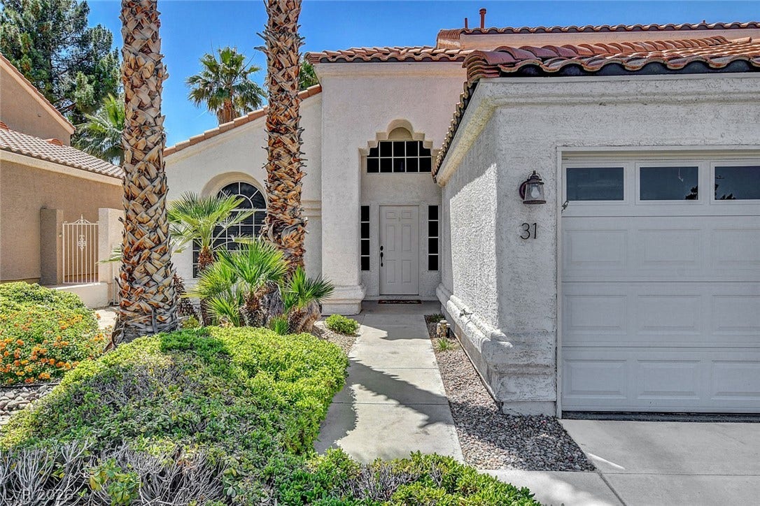 31 Antero Drive, Henderson, NV 89074 Lush landscaping and tall palms frame the inviting stucco exterior and arched entry.