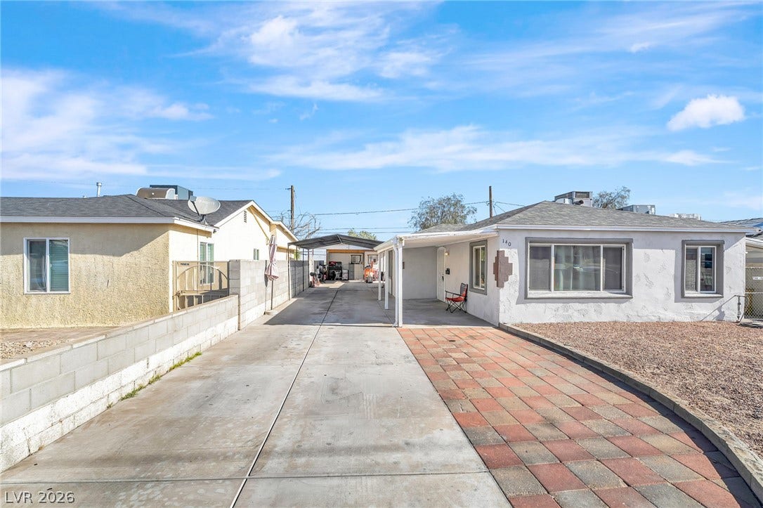 A well-maintained facade with a covered parking area and a mix of concrete and paver driveway.