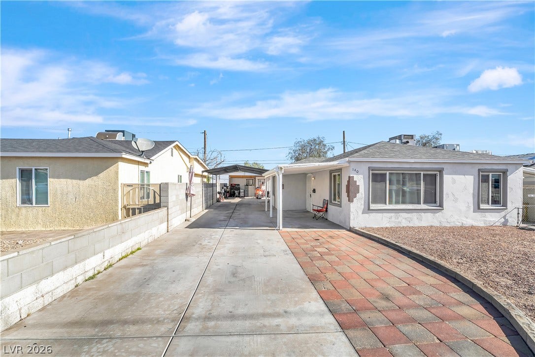 A lengthy concrete driveway leads to a covered carport, offering ample off-street parking for multiple vehicles.