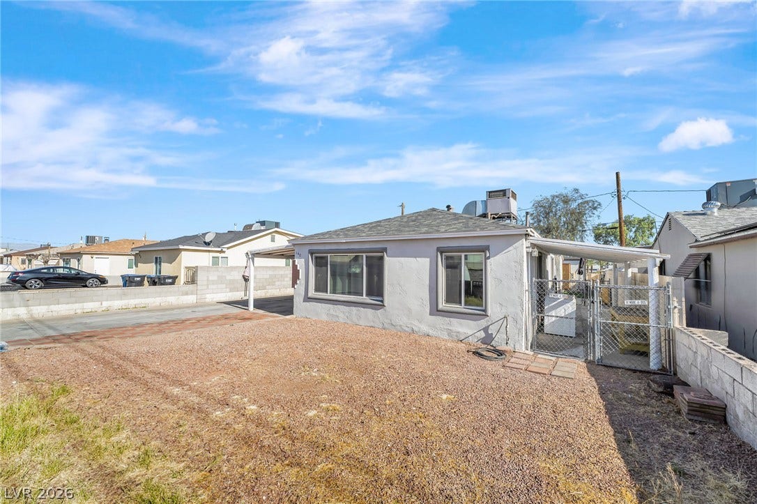 A modest stucco residence with a car port and private yard, nestled under a bright sky.
