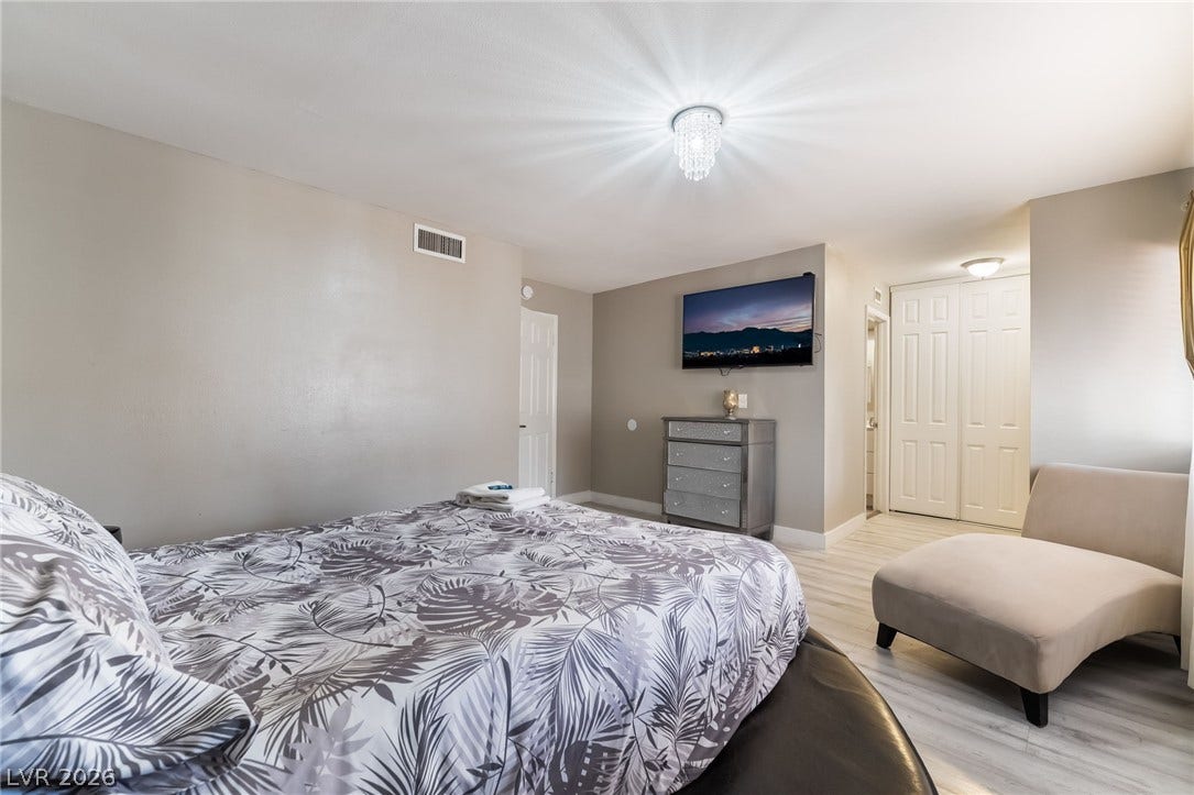 3111 Belvedere Drive, Henderson, NV 89014 A spacious sleeping quarter features light wood-look flooring and a contemporary chandelier.