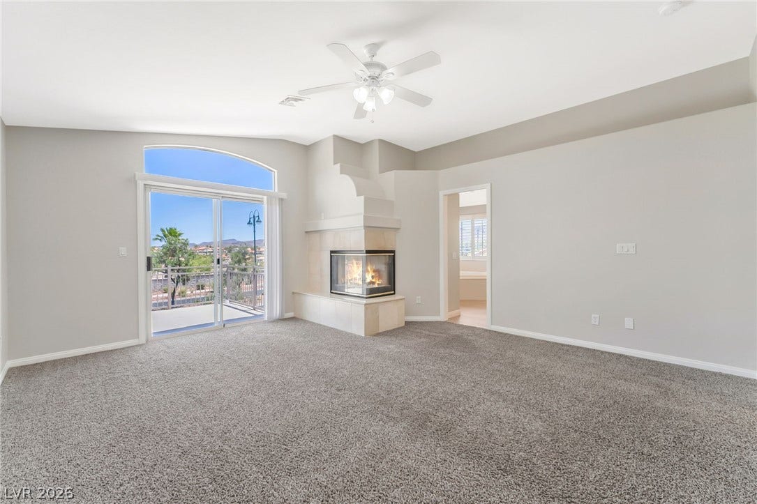 1278 Autumn Wind Way, Henderson, NV 89052 A spacious primary bedroom with a corner fireplace, private balcony access, and a ceiling fan.