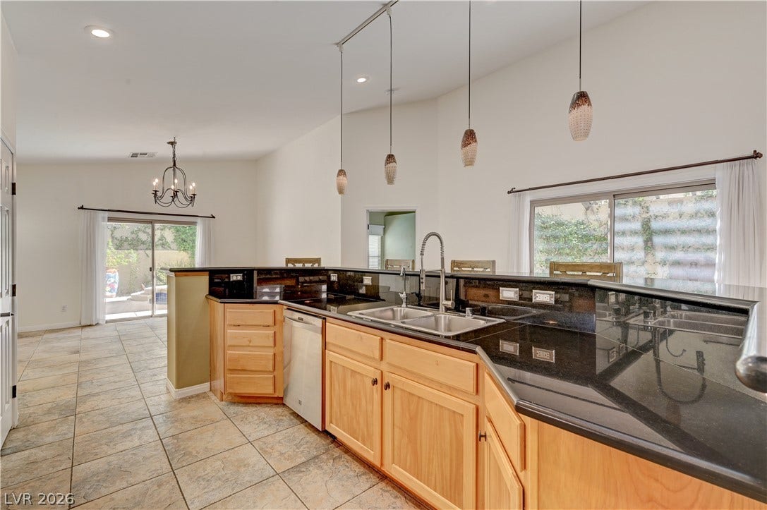 115 Cora Hills Court, Las Vegas, NV 89148 Granite counters and light wood cabinetry define this well-appointed kitchen, flowing seamlessly into a dining space with patio access.