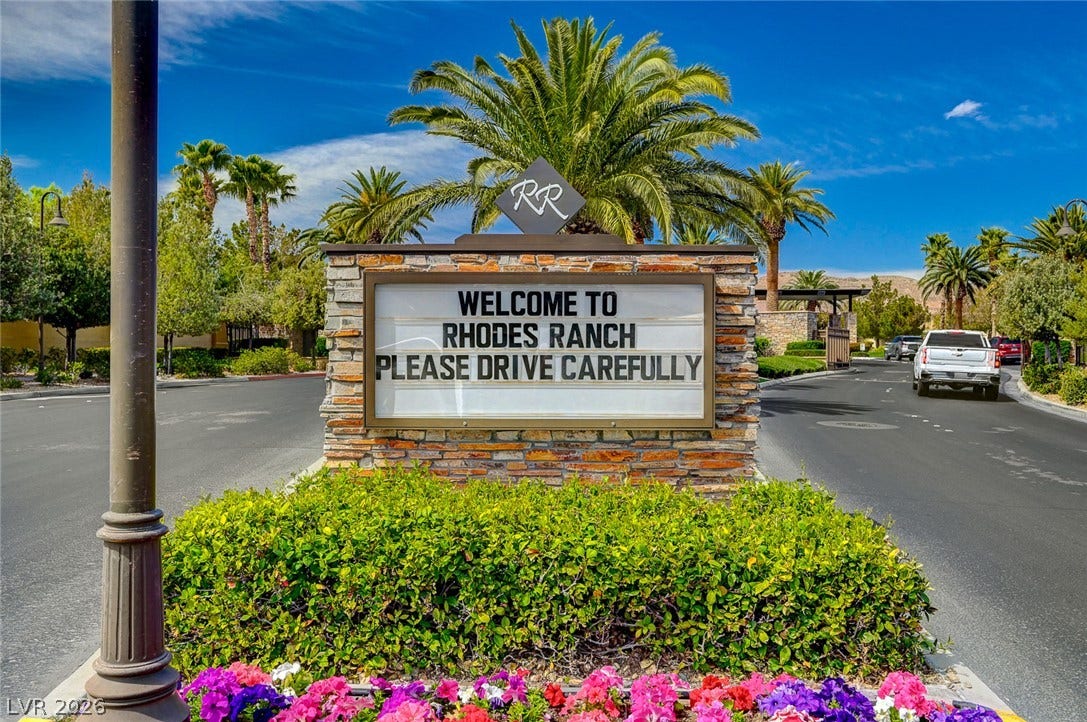 115 Cora Hills Court, Las Vegas, NV 89148 Enter a community through a stone monument sign, flanked by lush landscaping under a bright sky.