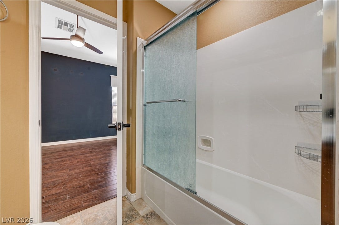 115 Cora Hills Court, Las Vegas, NV 89148 A pristine tub and shower enclosure with sliding glass doors, adjoining a room with rich wood-look flooring.